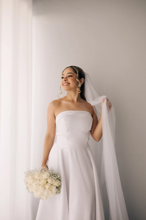 Noiva com véu e buquê de rosas brancas, make luminosa